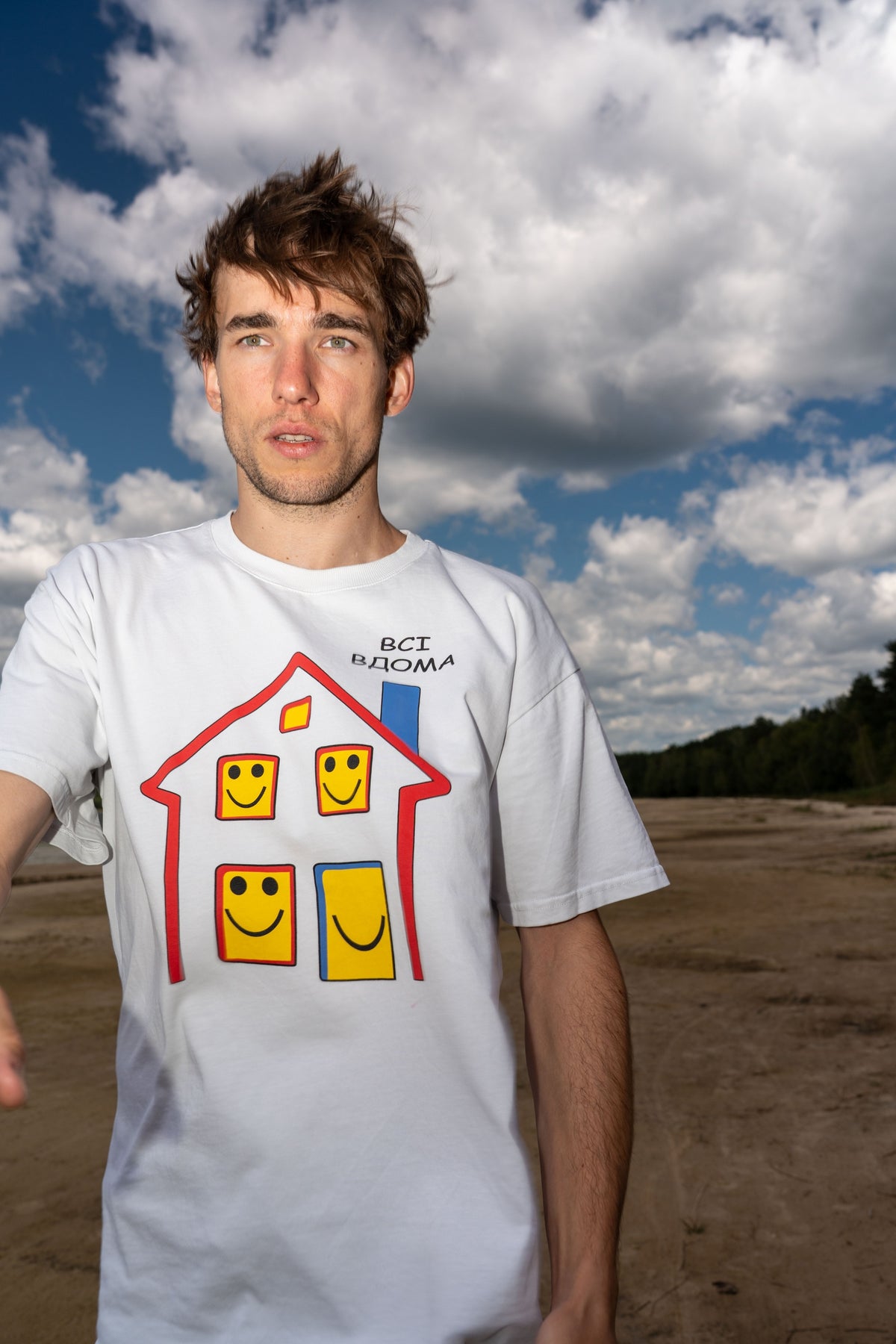 Man wearing the white Everyone’s Home T-shirt with its illustrated print
